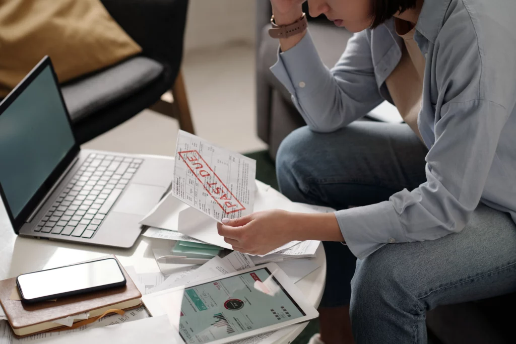 Worried person reviewing overdue bill amid financial documents and devices.